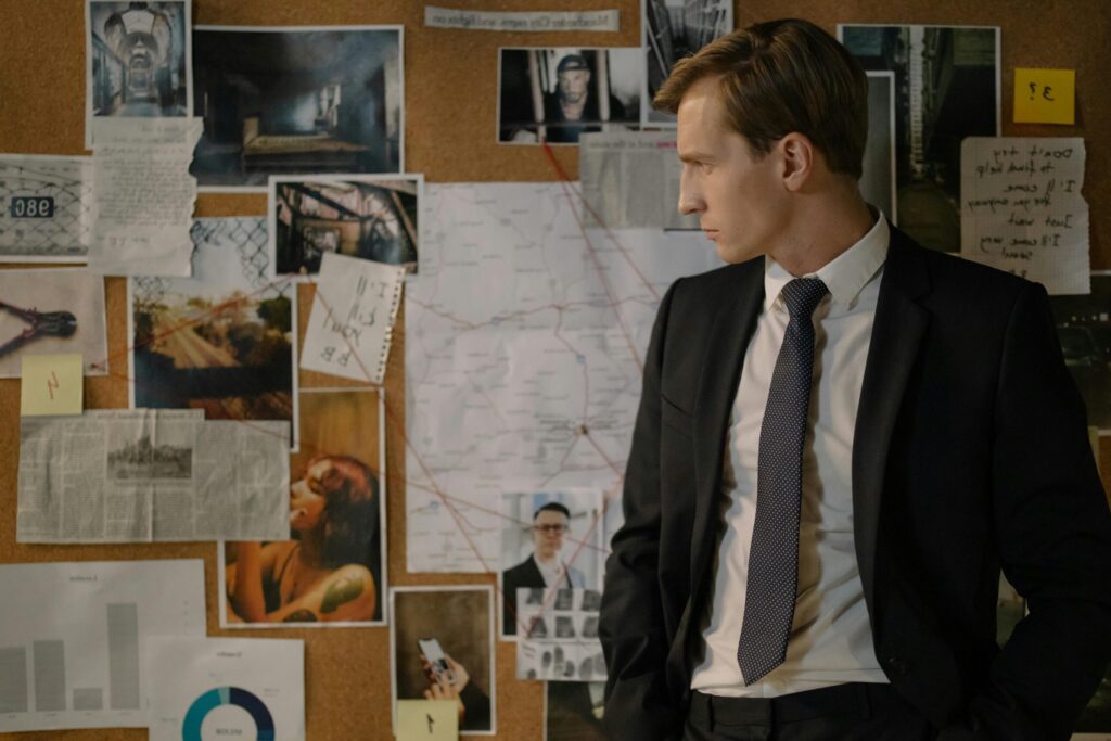 Detective in suit examining evidence on cork board during investigation process.